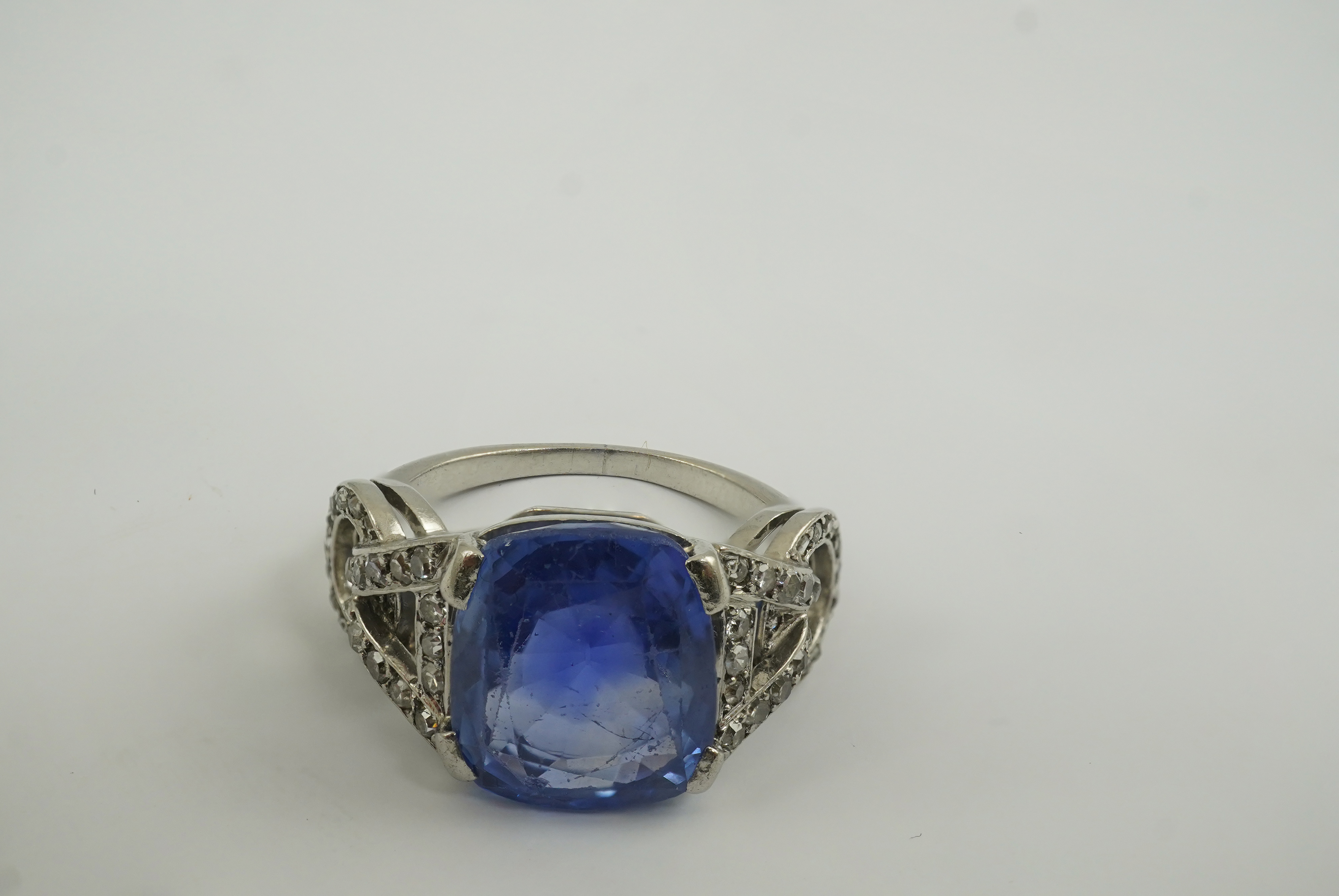 A mid to late 20th century platinum and single stone tapered cushion cut sapphire set dress ring, with diamond chip set pierced shoulders